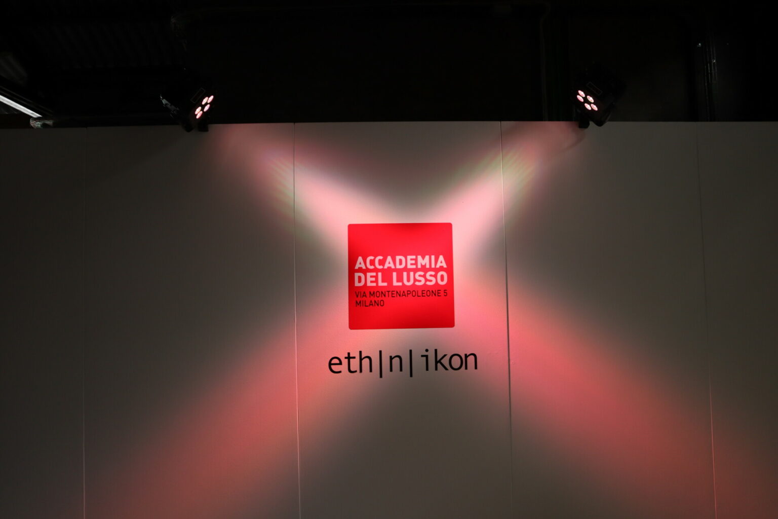 a red sign with white text on a white wall with two spotlights